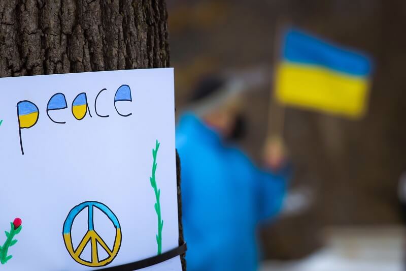 A paper with Peace written and a person on background with the Ukraine flag